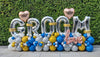 Silver GROOM balloon letters with personalised hearts, rose gold LOVE lettering and blue, gold, white and silver balloons placed outdoor.