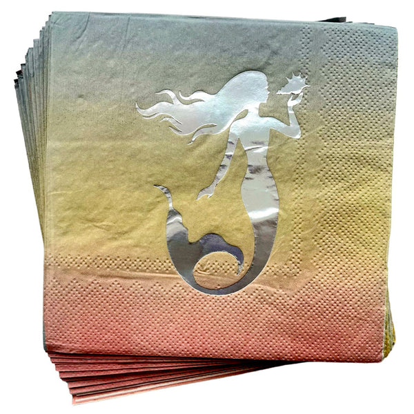 Folded mermaid paper napkins featuring a metallic looking mermaid silhouette against a pastel gradient background for an ocean inspired party setting.