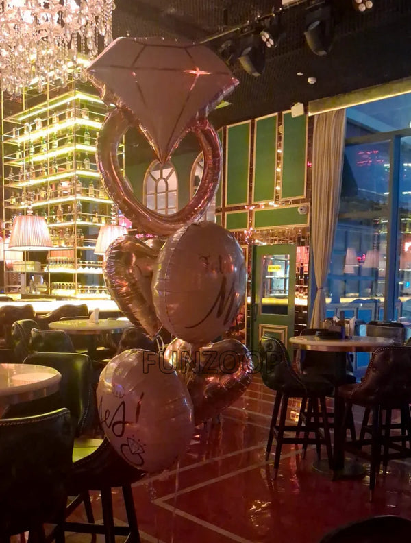 Rose gold diamond ring helium bouquet with two heart balloons and two round bridal-themed foil balloons at a restaurant.