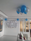 Ceiling balloon home decoration with blue and silver-toned balloons, curling ribbons and an add-on birthday banner in a living room.