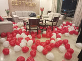 Scarlet-red and white floor balloons with heart accents beneath gold birthday letters in a living room