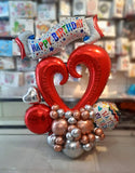 Red open-heart birthday balloon centrepiece with a multicolour banner and rose-gold and silver balloon base.